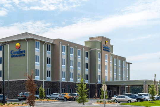 Wide shot of the Comfort Inn & Suites Valdosta with cars in the parking lot and a a blue cloudy sky overhead.