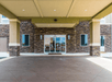 The front covered entrance to the Comfort Inn & Suites Valdosta with rock on the bottom half of the wall on a sunny day.