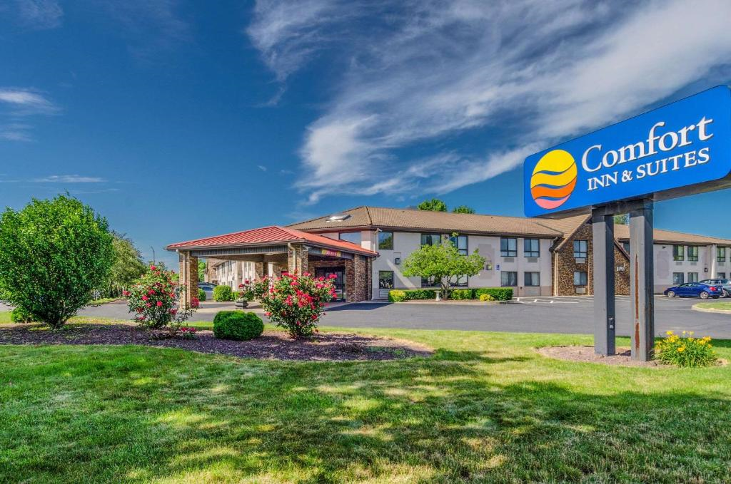 Exterior view of a Comfort Inn & Suites hotel with a lawn, trees, and a sign, under a partly cloudy blue sky.