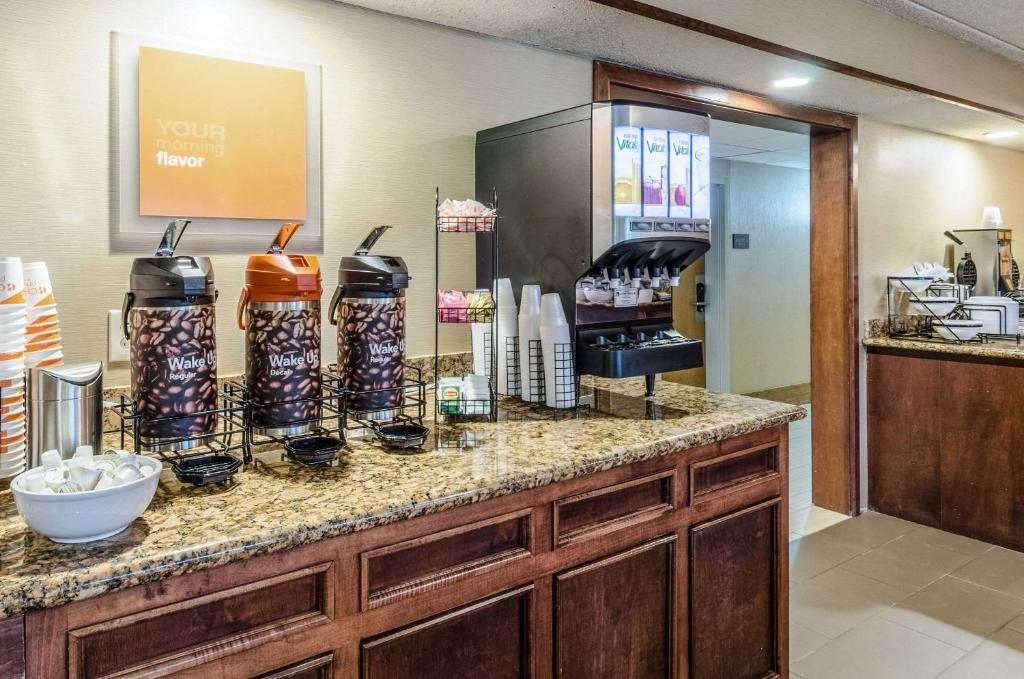 Hotel breakfast area with a granite counter featuring coffee dispensers, a juice machine, cups, and condiments. A cabinet with additional breakfast items is visible in the background.