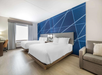 Hotel room with two double beds, modern blue geometric accent wall, a desk, window with gray curtains, and a couch with striped pillow.