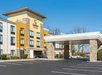Exterior view of a Comfort Suites hotel, featuring a stone facade and covered entrance, with a car parked in the driveway on a clear day.