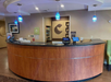 Hotel front desk with a wooden counter, two computer monitors, blue pendant lights, and wall signage in the background.