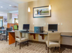 A hotel business center with two chairs, two computers, a printer, and framed artwork on a beige wall.
