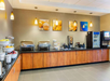 Breakfast buffet with fruit baskets, chafing dishes, cereal dispensers, and drink machines in a hotel dining area.