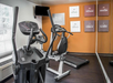 A small gym with two elliptical machines, a wall-mounted TV, and motivational posters on an orange and white wall.