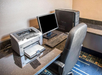 Office setup with a desktop computer, keyboard, monitor, and printer on a dark granite desk, accompanied by a black chair.