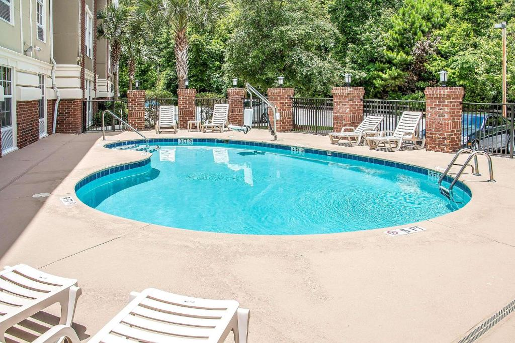 Outdoor swimming pool surrounded by lounge chairs and trees, with brick pillars and a metal fence lining the perimeter.
