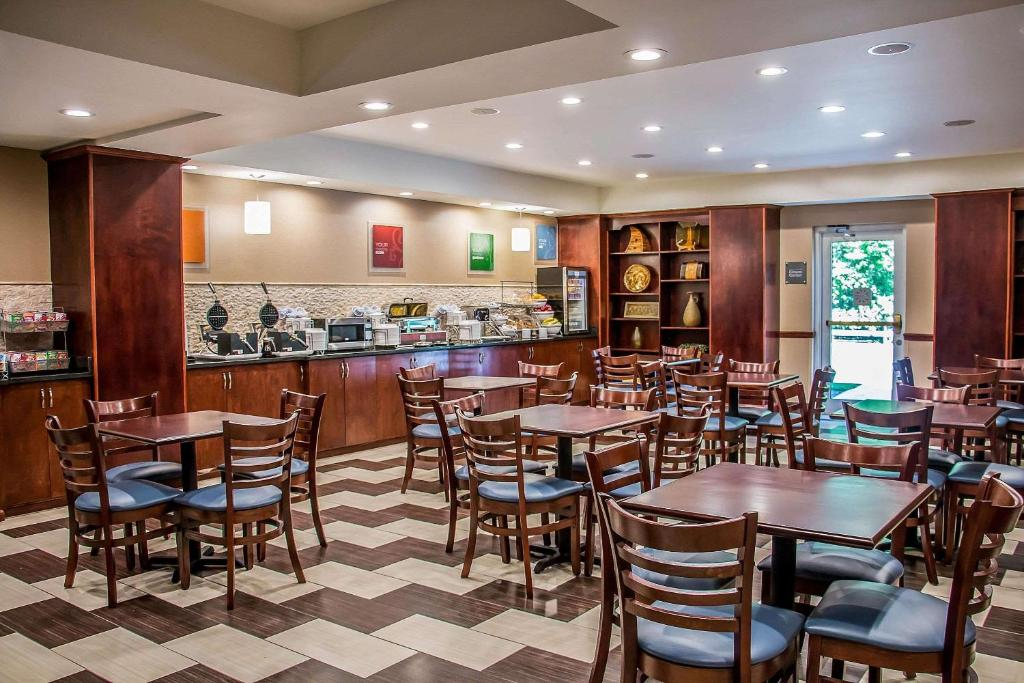 A dining area with multiple wooden tables and chairs. The background features a buffet counter with breakfast items under warm lighting.