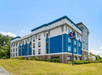 Four-story Comfort Suites hotel with blue and white exterior, surrounded by greenery under a clear sky.