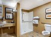 Accessible hotel bathroom with walk-in shower, wall-mounted sink, toilet with grab bars, and neatly stacked towels.