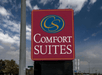Close up of the red and blue sign for the Comfort Suites New Braunfels on a sunny day with clouds in the sky overhead.