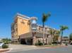 A three-story Comfort Suites hotel with palm trees in the foreground and a clear blue sky above.