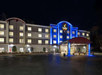 A four-story hotel at night with illuminated exterior lights, featuring a covered entrance and well-lit windows.