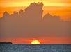 Sunset over the ocean with a vibrant orange sky and clouds, as the sun sets near the horizon.