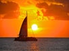 Sailboat on the ocean silhouetted against a vibrant sunset with orange and yellow clouds.