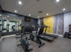 A modern gym room with two treadmills, two stationary bikes, free weights, a large wall mirror, and colorful wall decor.
