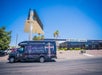 A black van with "Count's Kustoms" graphics is parked in front of the Shelby American building on a sunny day with clear blue skies.