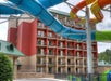 A multi-story hotel building with balconies is seen in the background. In the foreground, there are colorful water slides, including blue, yellow, and green tubes.