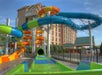 Colorful water slides at an outdoor water park near a hotel building under a clear blue sky.