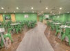 A dining area with green walls and matching green chairs around metal tables. The room has a polished wood and tile floor with overhead lighting. Art pieces are displayed on the walls.