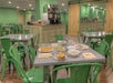 Cafeteria setting with green chairs and tables, featuring plates of breakfast items like waffles, fruit, and toast, along with cups and cutlery on a table.