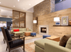 A lounge area with two couches, chairs, ottomans, coffee tables, and lamp in front of a fireplace with a breakfast area in the backgorund.