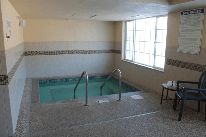 A small indoor in-ground hottub with a large window to the right and a table and chair in front of it.