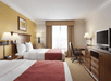 Two queen beds, bright lamps, work desk and a flat-screen TV inside a guest room.