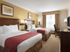 Two queen beds, bright lamps, work desk and a flat-screen TV inside a guest room.