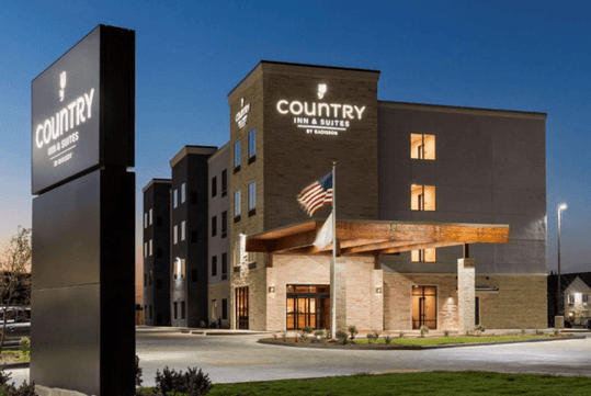 Ground view looking at the Country Inn & Suites at dusk with the sun setting behind it in New Braunfels, Texas.