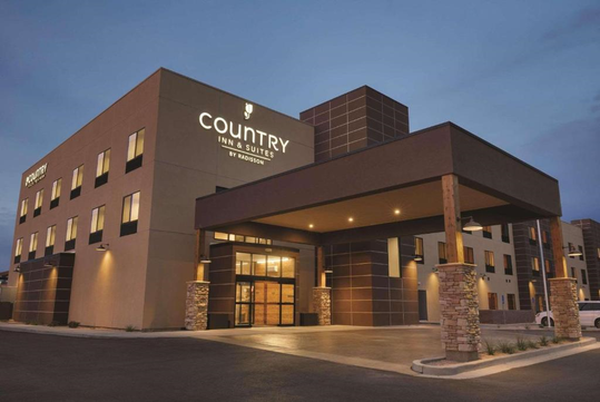 Modern hotel building with a large entrance and illuminated signage reading "Country Inn & Suites by Radisson" during early evening.