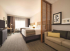 Hotel room with two beds, a desk, and a beige sofa. A wooden partition separates the beds and sofa. Framed art hangs on the wall above the sofa. A TV is on a dresser near the desk.