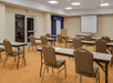 Conference room with tan carpeting, several tables, brown chairs, a projector screen, and a podium. The room is well-lit with overhead lighting.