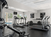 A gym room with treadmills, a bench, and exercise equipment. Mirrors on the wall, windows showing trees outside.