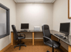 Small office with two workstations, each featuring a computer and chair, separated by a printer on a shared desk.