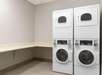 A laundry room with two stacked white washer-dryer units, a beige countertop, and light-colored walls.