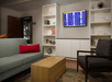 A lounge area with a green couch, gray chairs, a light wooden coffee table. and a TV mounted on the wall with built in shelves full of decor on both sides.