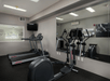 A small fitness center with a stationary bike in front of a mirror and two treadmills to its left with a small TV mounted over them.