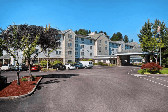 The front exterior and parking lot of the Country Inn & Suites by Radisson with small trees and bushes in the landscaping on a bright and sunny day.