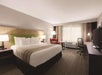 One king bed, seating area, TV, and work desk with chair inside a guest room.