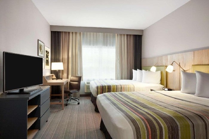 Two queen beds, TV, and work desk with chair inside a guest room.