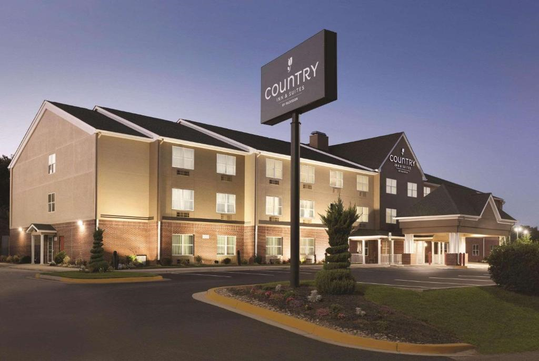 Hotel exterior with a large sign that says "Country Inn & Suites." The building is three stories tall, with a well-lit entrance and manicured landscaping in the foreground.