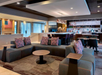 Modern hotel lobby with a seating area featuring gray couches and red-patterned pillows. A Starbucks counter is visible in the background.