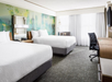 Two double beds, telephone, flat-screen TV, and a work desk inside a bright guest room.