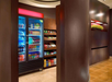 A hotel snack area featuring a refrigerated display with drinks and shelves stocked with snacks and chips.