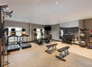 A fitness room with treadmills, exercise bikes, weight benches, dumbbells, and medicine balls. A large mirror and a wall-mounted TV are present.