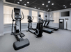 A modern gym with three elliptical machines, two treadmills, a wall clock, a TV, and a storage unit with towels under bright ceiling lights.