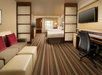Two queen beds and a seating area with a sofa bed, work desk and two flat-screen TVs inside a guest room.