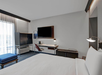Modern hotel room with a neatly made bed, wall-mounted TV, desk with chair, and large window with sheer curtains.